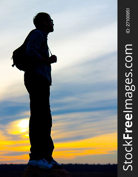 Silhouette of a man standing with a backpack or satchel on his back against a vivid orange sunset sky with copyspace. Silhouette of a man standing with a backpack or satchel on his back against a vivid orange sunset sky with copyspace