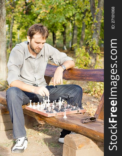 Serious male chess player sitting on a wooden bench with the chess board in front of him making a move. Serious male chess player sitting on a wooden bench with the chess board in front of him making a move