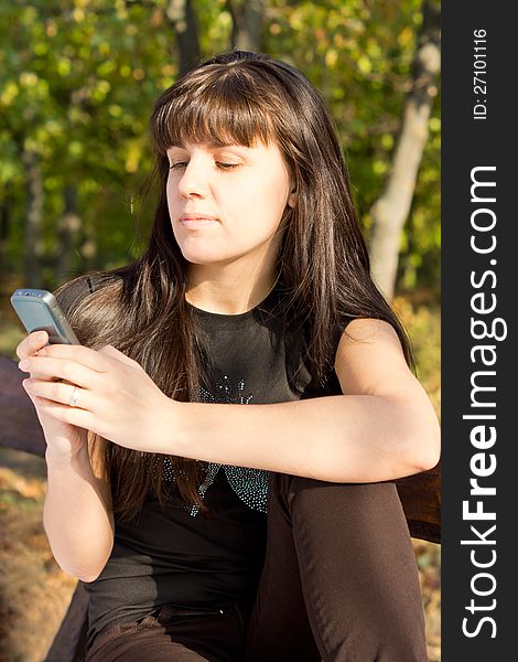 Young woman standing outdoors in sunny woodland reading a text message on the screen of her mobile phone. Young woman standing outdoors in sunny woodland reading a text message on the screen of her mobile phone