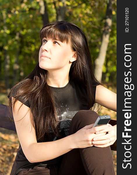 Attractive young woman staring up at the sky daydreaming while waiting for a call on her mobile phone. Attractive young woman staring up at the sky daydreaming while waiting for a call on her mobile phone