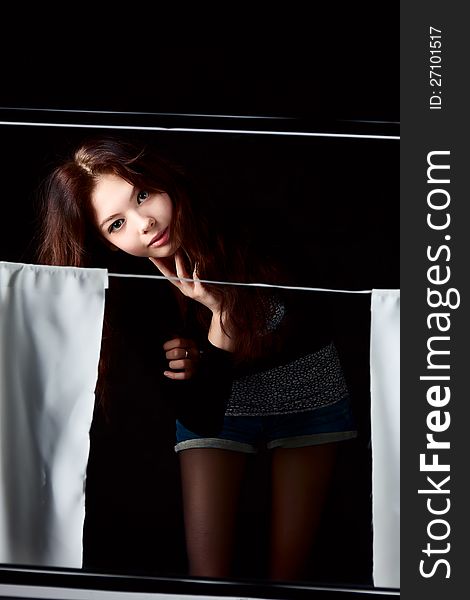 Young girl in the window with the curtains dark background. Young girl in the window with the curtains dark background