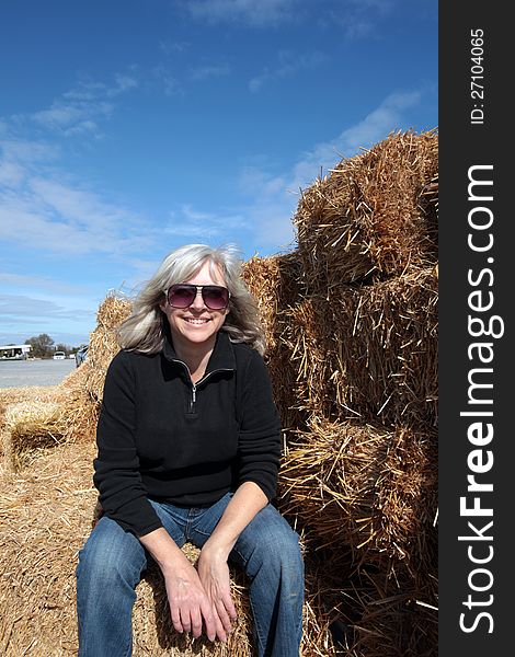 Attractive middle aged woman sits enjoying the sun on straw bales on a beautiful fall day. Attractive middle aged woman sits enjoying the sun on straw bales on a beautiful fall day.