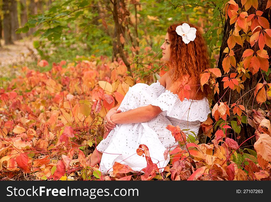 Beautiful red-haired young woman, wearing in white dress or the bride and decoration in form of flower on her head among red leaves in autumn forest.and dreaming. symbol of autumn. Beautiful red-haired young woman, wearing in white dress or the bride and decoration in form of flower on her head among red leaves in autumn forest.and dreaming. symbol of autumn