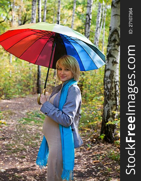 Beautiful young fashion pregnant woman walking in the park with colorful rainbow umbrella. Beautiful young fashion pregnant woman walking in the park with colorful rainbow umbrella