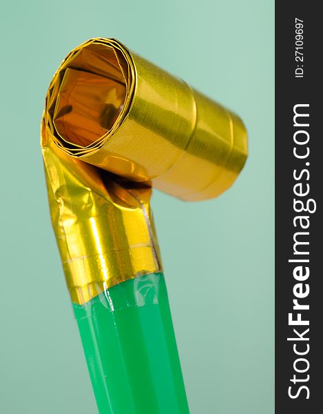 A golden folded party blowout (noise maker) on a green background â€“ vertical orientation. A golden folded party blowout (noise maker) on a green background â€“ vertical orientation