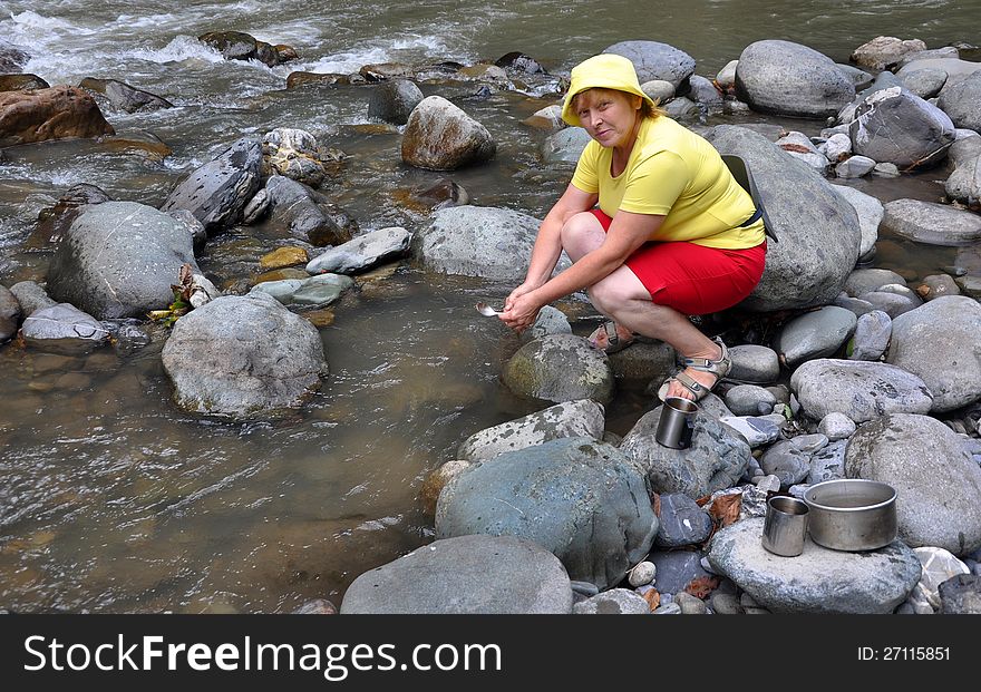 Adult female tourist washing utensil in mountains river (Russia, Sochi National Park)
