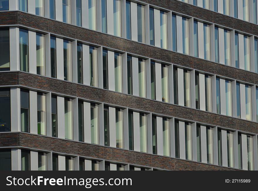 The facade of a modern office building with vertical white panels and horizontal red brown brick stripes