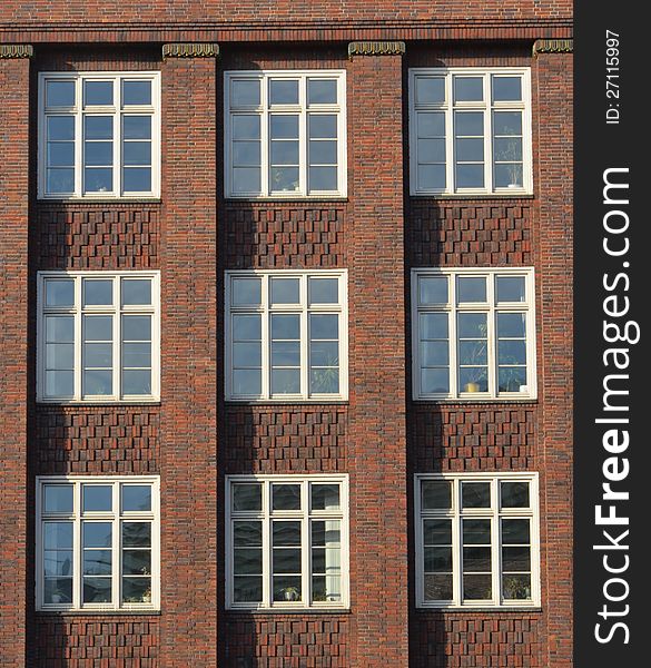Nine square windows are set in a red brick face ornamented with square columns and a pattern of bricks receding and protruding in squares. Nine square windows are set in a red brick face ornamented with square columns and a pattern of bricks receding and protruding in squares.