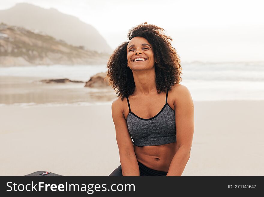 Happy woman with closed eyes sitting on a beach after yoga exercises