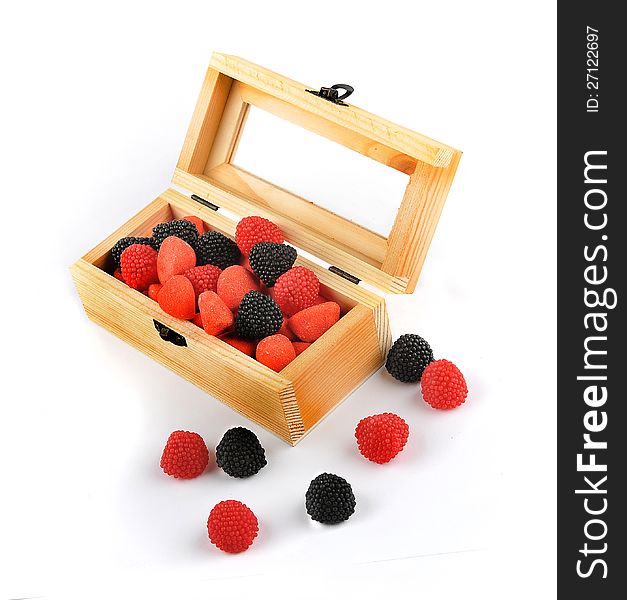 A wooden box with candies of black and red colors isolated on a white background. Some candies are outside the box. A wooden box with candies of black and red colors isolated on a white background. Some candies are outside the box.