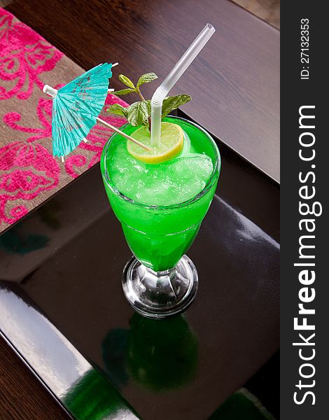 Brightly lighted and Green drink with ice with lemon and mint ( kiwi , mint ) and green umbrella. Brightly lighted and Green drink with ice with lemon and mint ( kiwi , mint ) and green umbrella