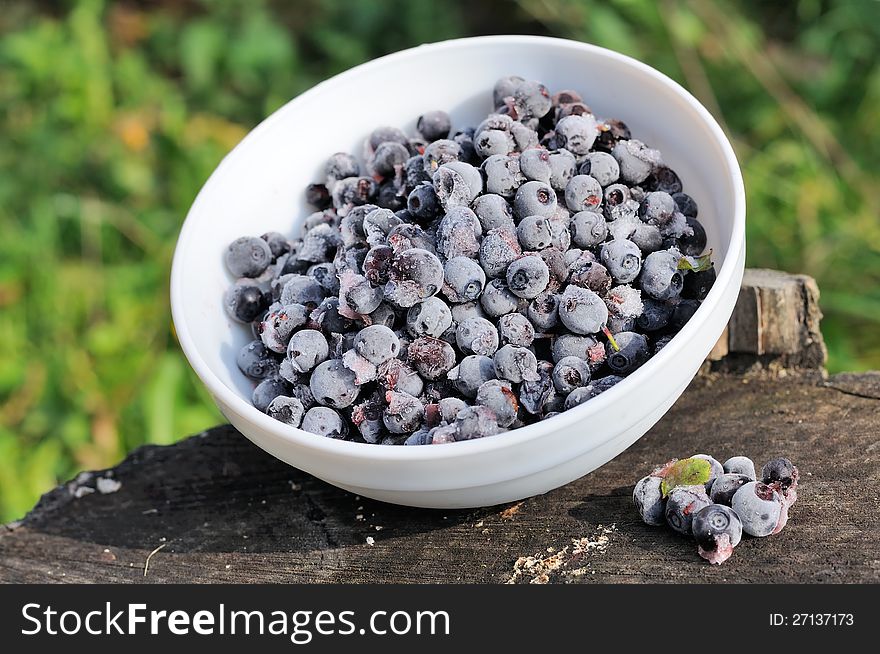 Frozen bilberries in a ceramic bowl on a tree stump. Frozen bilberries in a ceramic bowl on a tree stump