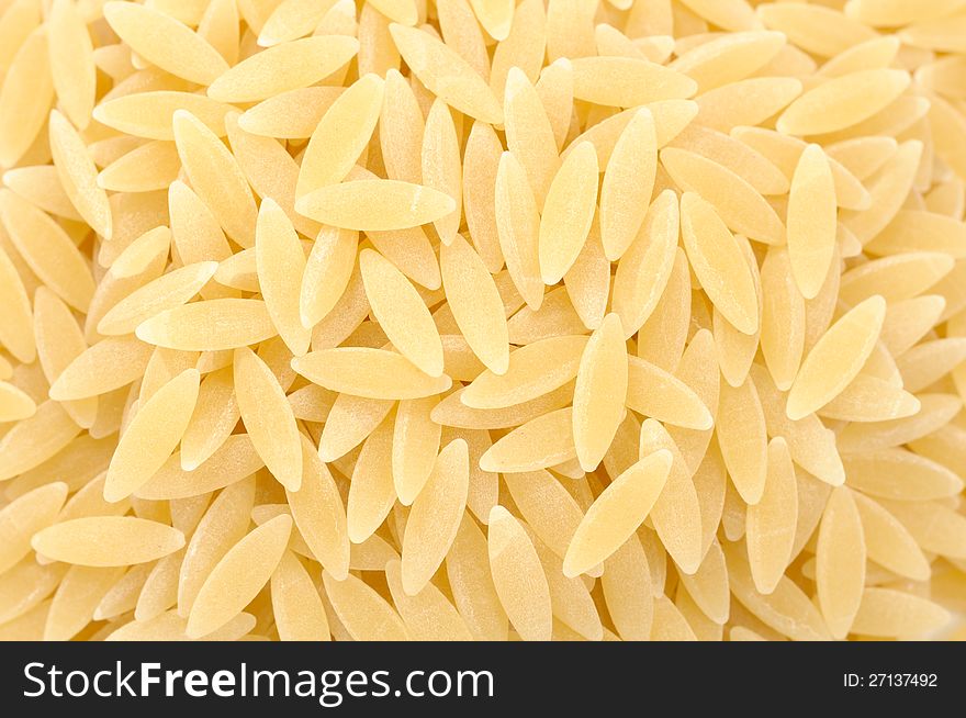 A close-up shot of rice-shaped orzo (risoni) pasta as a background. A close-up shot of rice-shaped orzo (risoni) pasta as a background