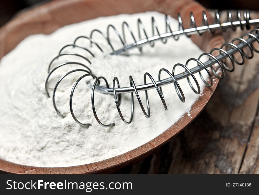 Wheat flour and whisk on wooden background