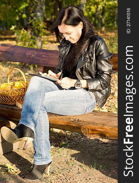 Woman sitting on a wooden bench in the country with a basket of apples using her tablet. Woman sitting on a wooden bench in the country with a basket of apples using her tablet