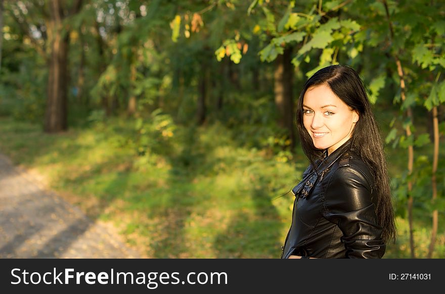 Smiling young woman in a leather jacket walking through woodland in evening light with copyspace. Smiling young woman in a leather jacket walking through woodland in evening light with copyspace