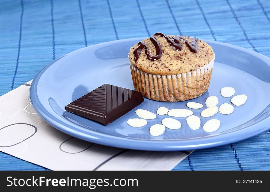 Closeup of a muffin with dark chocolate and almond chips on a blue dessert plate. Closeup of a muffin with dark chocolate and almond chips on a blue dessert plate