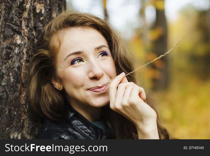Portrait of smiling girl sitting near the tree in red autumn forest