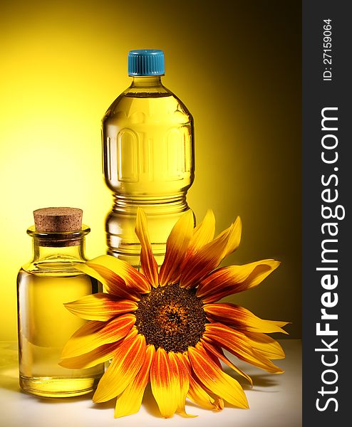 Cooking oil in a plastic and glass bottles with sunflower on a dark yellow background. Cooking oil in a plastic and glass bottles with sunflower on a dark yellow background.