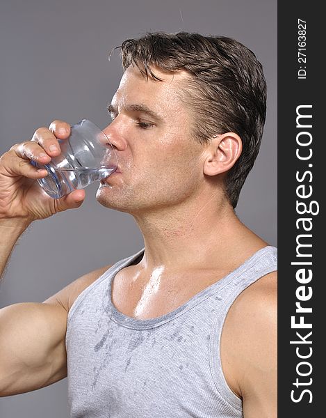 Thirsty sweaty muscular Caucasian man drinks glass of water. Thirsty sweaty muscular Caucasian man drinks glass of water