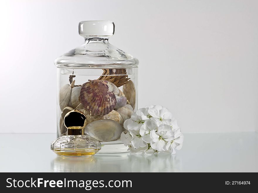 A glass of shells and a bottle of perfume is decorated with a white flower. A glass of shells and a bottle of perfume is decorated with a white flower.