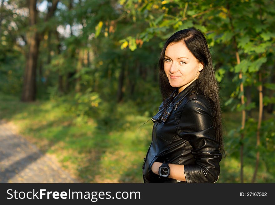 Happy woman in a leather jacket standing with the evening sun in her face in woodland. Happy woman in a leather jacket standing with the evening sun in her face in woodland