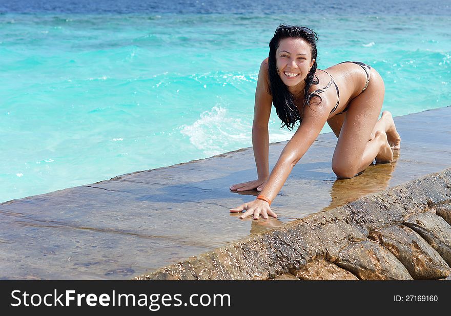 young brunette woman in a bikini crawling along a sea wall with clear blue water after enjoying a refreshing swim. young brunette woman in a bikini crawling along a sea wall with clear blue water after enjoying a refreshing swim