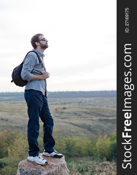 Man exploring with a backpack standing on top of a rock in open countryside with copyspace