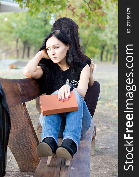 Bored women sitting on a rustic wooden bench in the countryside with her closed book in her hand staring off into space daydreaming. Bored women sitting on a rustic wooden bench in the countryside with her closed book in her hand staring off into space daydreaming