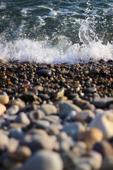 Splashing Waves On The Seashore. The Beach Is Made Of Small Colorful Pebbles. Sea Water Splashes Hitting The Stones. Royalty Free Stock Image