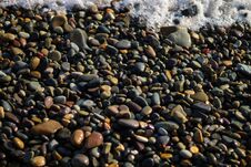 Wet Rocks By The Sea. The Beach Is Lined With Small Colorful Pebbles. Sea Foam From Small Waves. Stock Photography