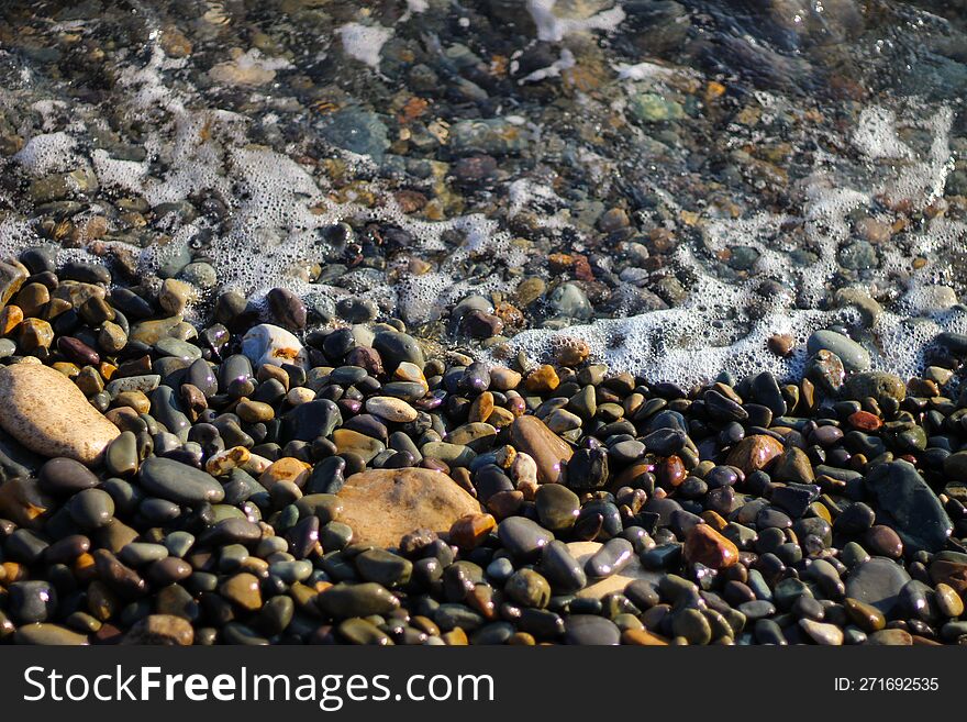 Crystal clear water on the seashore. The beach is lined with small colorful pebbles. Sea foam from the waves.