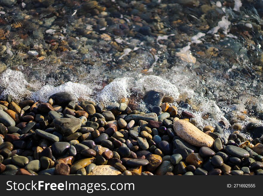 Crystal clear water on the seashore. The beach is lined with small colorful pebbles. Sea foam from the waves.