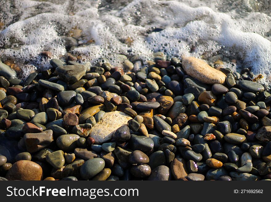 Sea foam from small waves. Crystal clear water on the seashore. The beach is lined with small colorful pebbles.