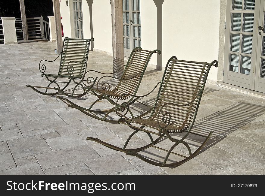 Three empty metal rocking chairs in front of the house. Three empty metal rocking chairs in front of the house.