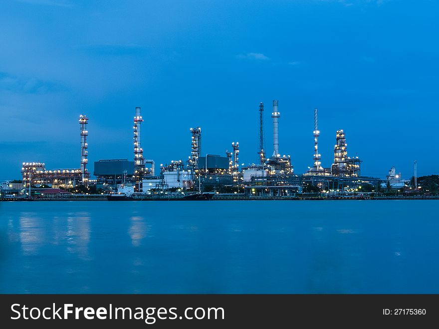 Petrol refinery station along river with light on at twilight. Petrol refinery station along river with light on at twilight