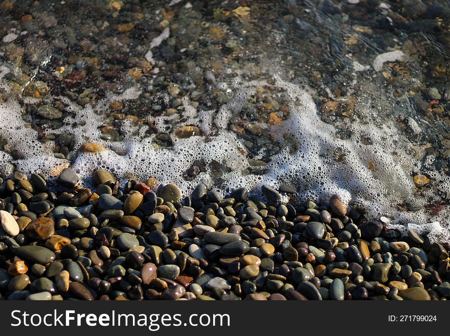 Crystal clear water on the seashore. Sea foam from small waves. The beach is lined with small colorful pebbles.