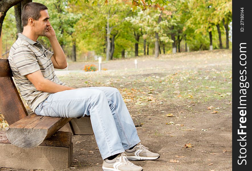 Middle-aged man sitting on a rustic wooden bench in a park chatting on his mobile phone. Middle-aged man sitting on a rustic wooden bench in a park chatting on his mobile phone