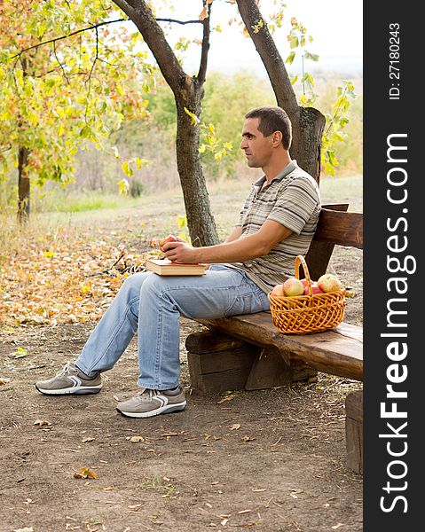 Attractive middle-aged man sitting on a rustic wooden bench outdoors eating apples with a basket full of fresh fruit at his side. Attractive middle-aged man sitting on a rustic wooden bench outdoors eating apples with a basket full of fresh fruit at his side