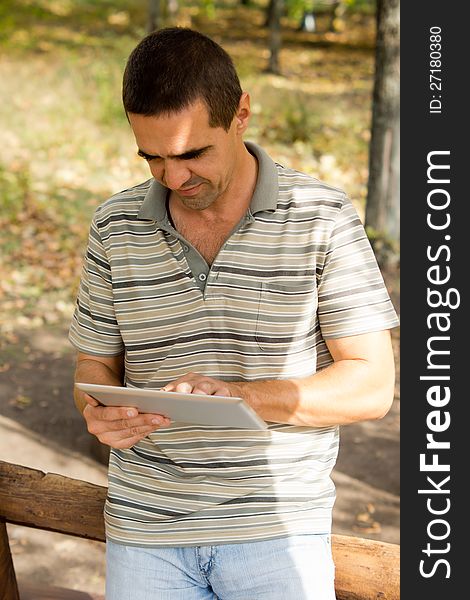 Casual middle-aged man standing typing on a touchscreen tablet that he is holding in his hand. Casual middle-aged man standing typing on a touchscreen tablet that he is holding in his hand