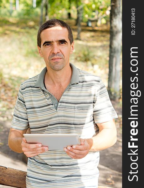 Attractive middle-aged man holding a tablet in his hands while looking at the camera, casual clothing in the garden