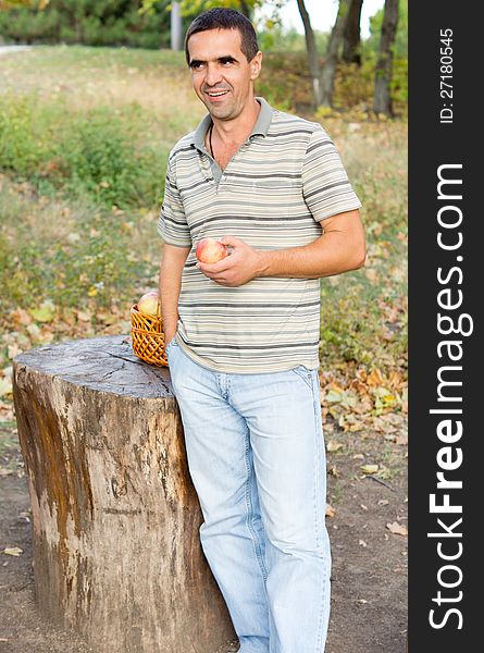 Smiling man standing alongside a sawn off tree trunk in the countryside with a fresh juicy apple in his hand. Smiling man standing alongside a sawn off tree trunk in the countryside with a fresh juicy apple in his hand