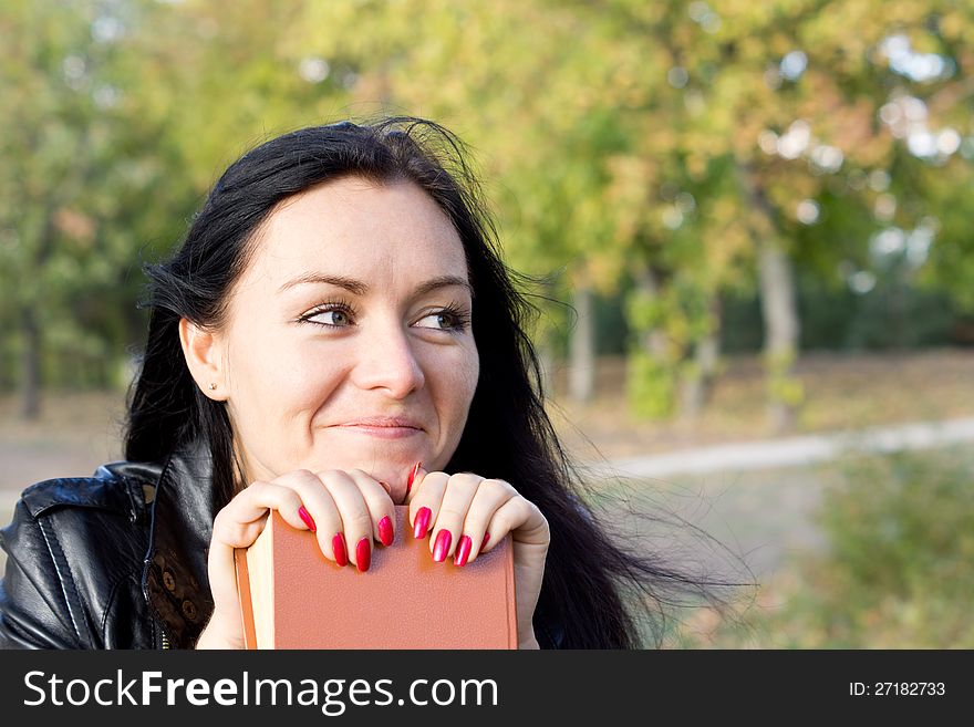 Smiling woman sitting outdoors in woodland resting her chin on a book with copyspace. Smiling woman sitting outdoors in woodland resting her chin on a book with copyspace