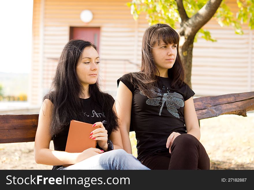 Two sad or thoughtful looking women sittng on a bench outdoors with a book. Two sad or thoughtful looking women sittng on a bench outdoors with a book.