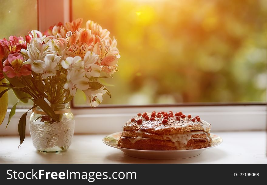 Against the background of the window is a cake with berries and a bouquet of flowers near. Against the background of the window is a cake with berries and a bouquet of flowers near