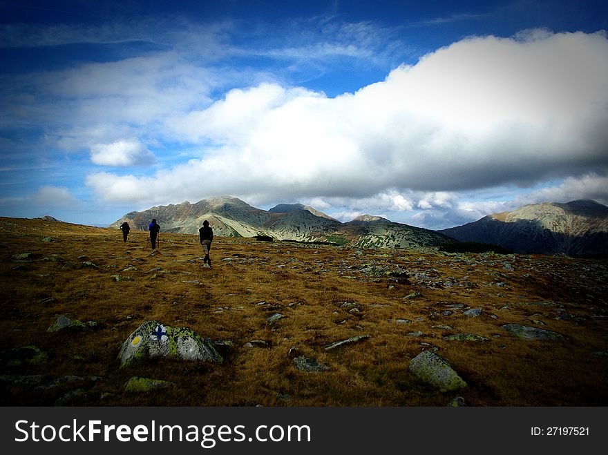 People walking on top of the 
mountain with other peaks 
in the background and a 
big cloud over their heads. People walking on top of the 
mountain with other peaks 
in the background and a 
big cloud over their heads