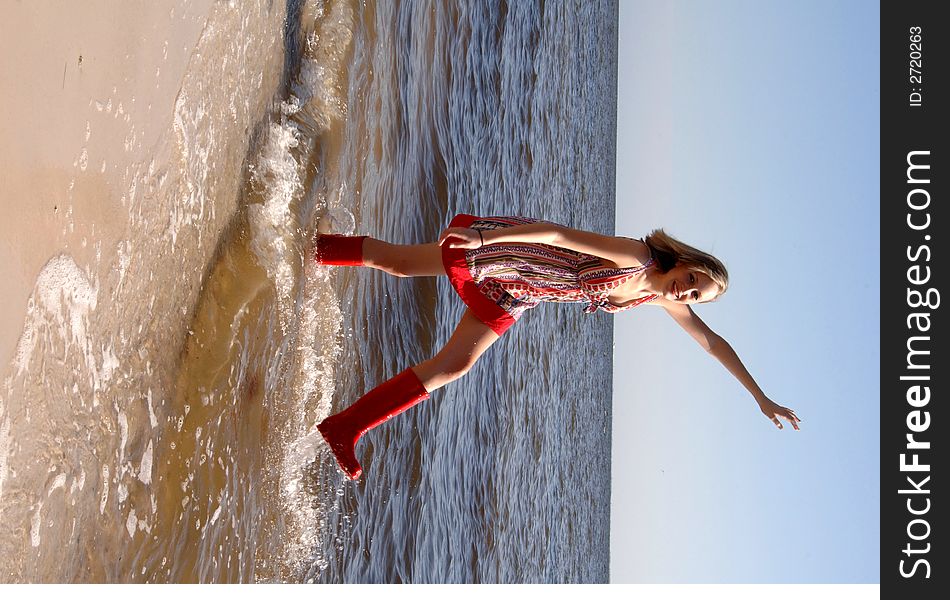 A pretty girl wearing a sundress and rubber boots splashing in the ocean. A pretty girl wearing a sundress and rubber boots splashing in the ocean
