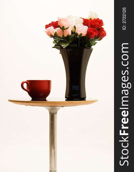 Small end table with a black vase full of red and pink roses beside a big red coffee mug. Small end table with a black vase full of red and pink roses beside a big red coffee mug