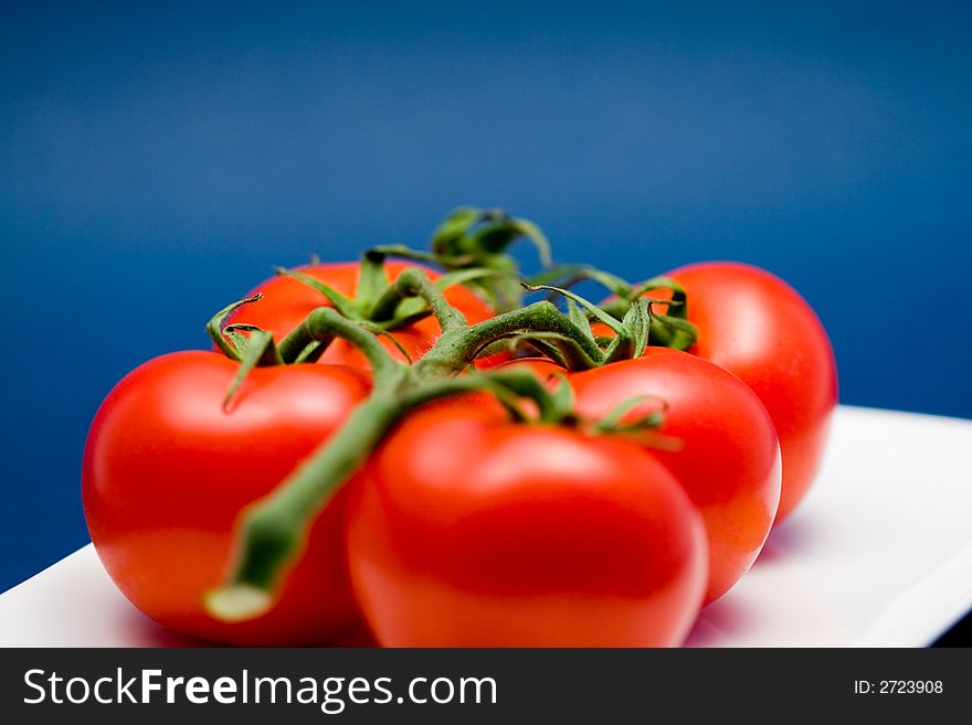 5 red tomatoes with stem on a white plate