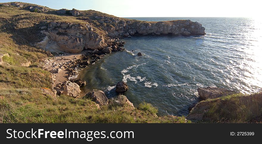 Small sea bay with sand beach and rocky borders and morning sun way highlight